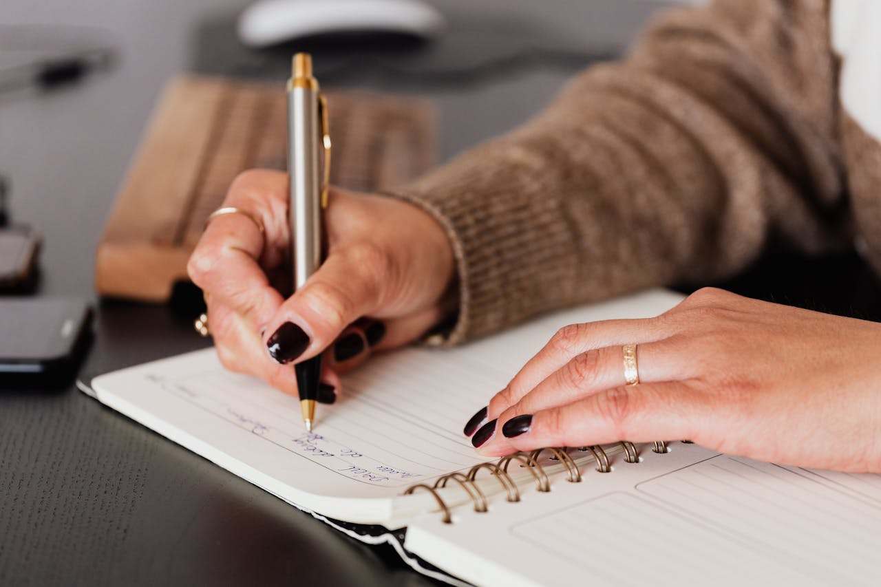 services-header Crop unrecognizable female with stylish manicure sitting at black desk with keyboard and smartphone and taking notes with silver pen in notepad