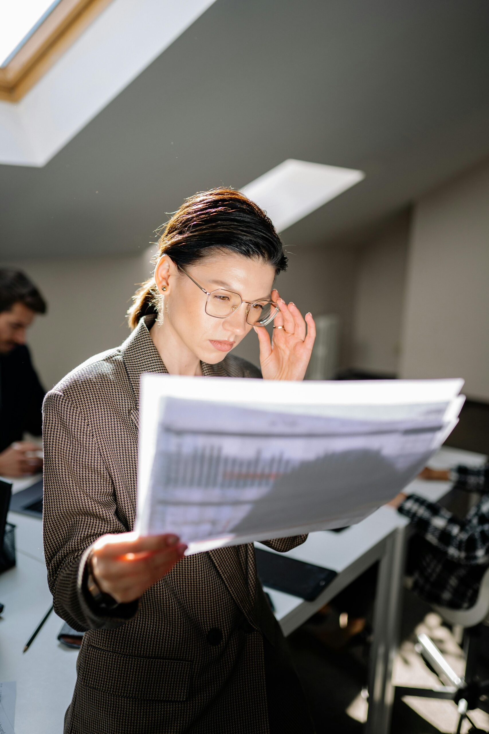 Caucasian woman in office reviewing financial papers under sunlight.